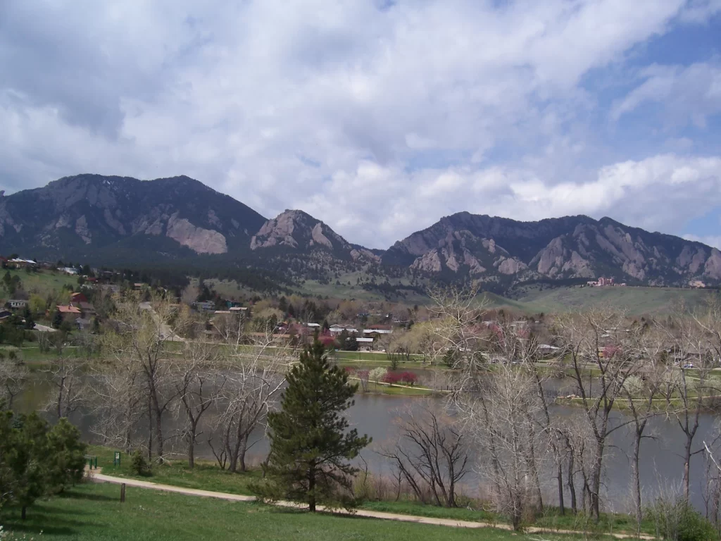 Photo of a reddish-brown mountain range with a greenish-blue lake and a city in the foreground